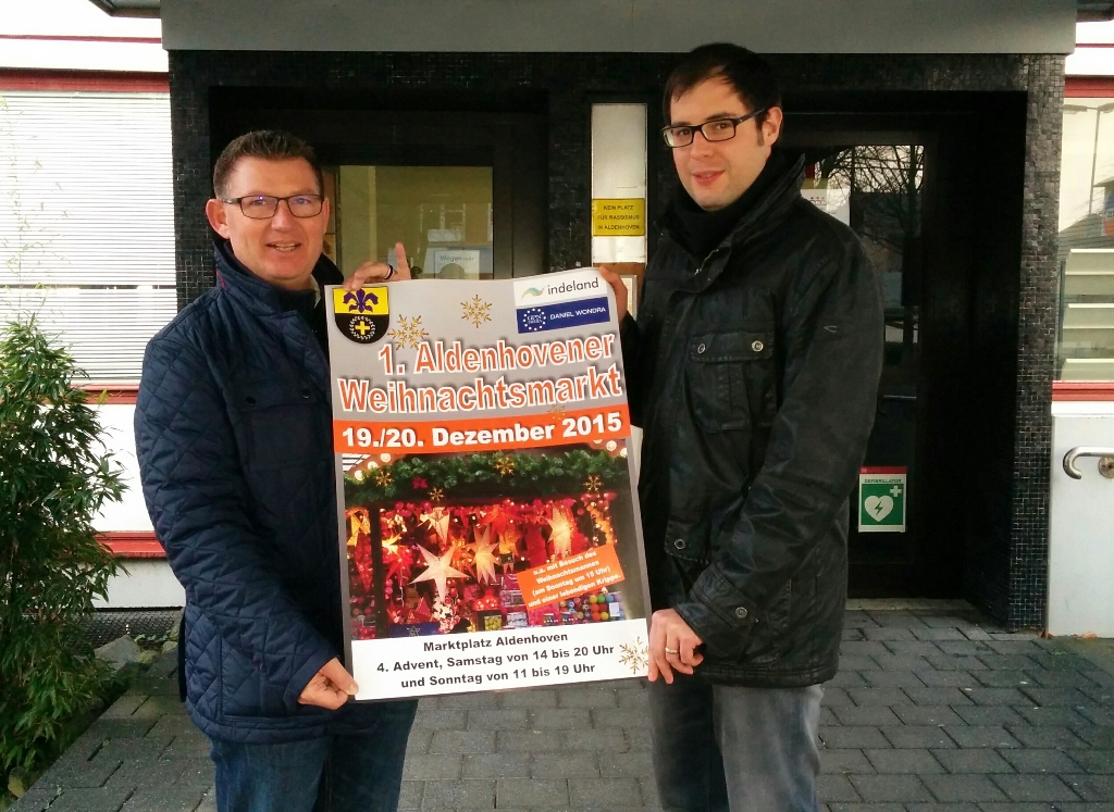 Bürgermeister Ralf Claßen und Marcel Dederichs (r.) präsentieren das Plakat zum Aldenhovener Weihnachtsmarkt, der am 4. Advent stattfindet.