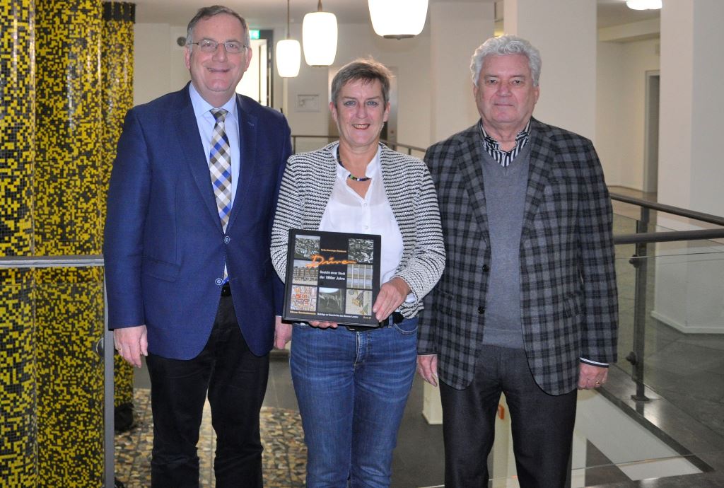 Foto: Von links: Bürgermeister Paul Larue, Autorin Heike Kussinger-Stanković, Leiterin der Unteren Denkmalbehörde der Stadt Düren, und  Dr. Helmut Irmen, Vorsitzender des Geschichtsvereins, freuen sich vor der Kulisse des 50er Jahre Rathauses über die Neuauflage.