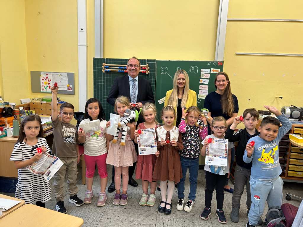 Leuchte auf deinem Schulweg: Landrat Dr. Ralf Nolten und Corinna Vonhasselt (Mitte) übergeben stellvertretend LED-Lampen für den Schulranzen an die Zebraklasse der KGS Südschule Düren. Mit dabei ist die kommissarische Schulleiterin Christiane Mörkens. Foto: Kreis Düren